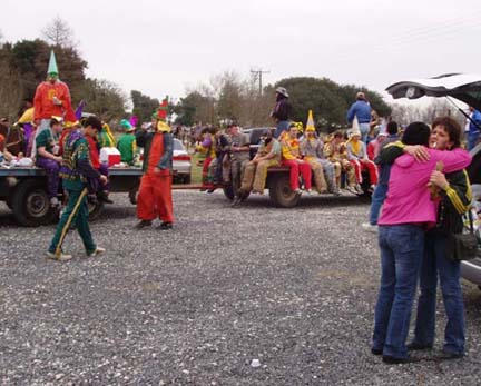 people in Mardi Gras costumes hugging and others riding on a wagon